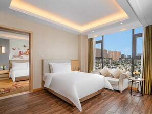 A hotel room with a large bed, a sofa, a small table, and a view of a cityscape. - Vienna International Hotel (Chengdu)