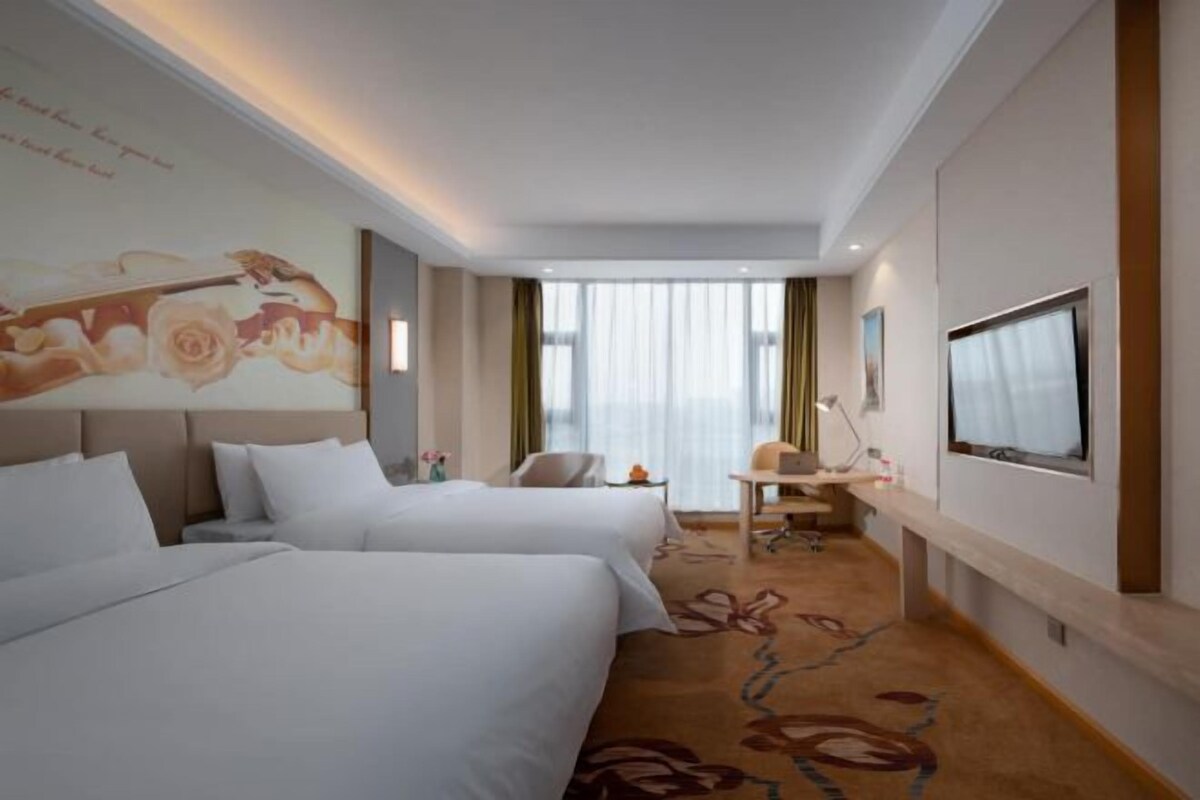 A hotel room with two beds, a desk, a chair, a TV, and a large window with curtains.