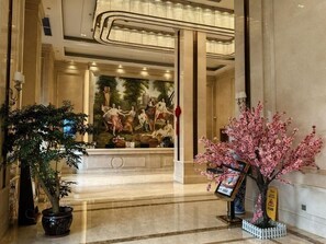 A lobby with a marble floor, a reception desk, a large mural, and potted plants. - Vienna International Hotel (Chengdu)