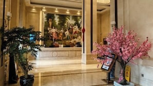 A lobby with a large mural, a reception desk, and two potted plants.