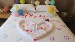 A hotel room with a bed adorned with a heart-shaped pillow and rose petals.
