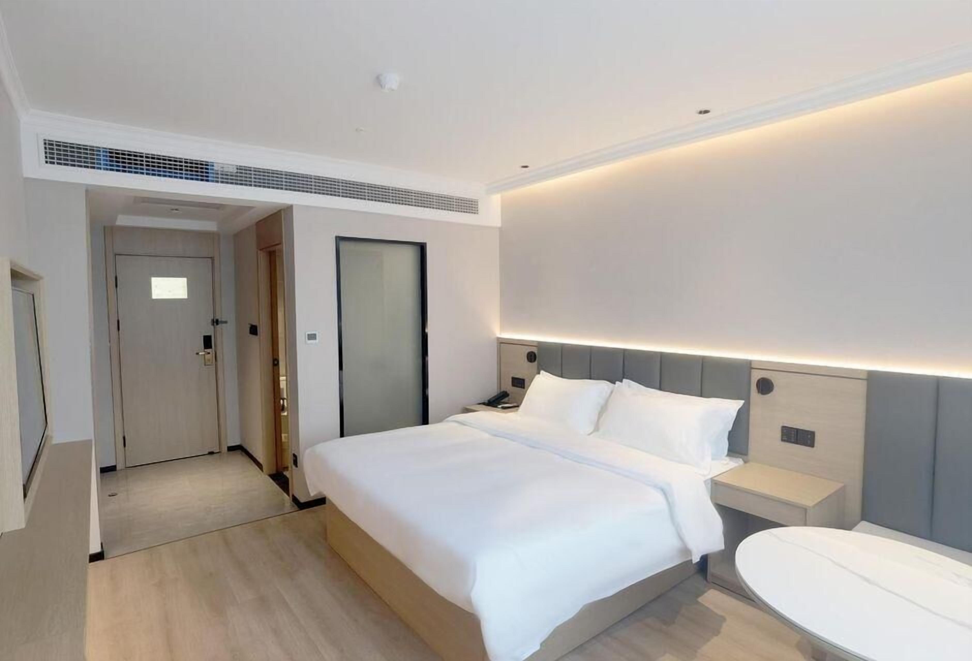 A modern hotel room with a large bed, bedside tables, a built-in desk, and a large mirror.