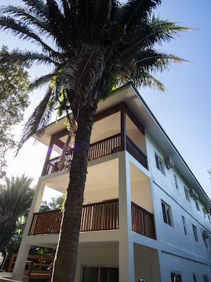 A multi-story building with balconies and a palm tree in front.