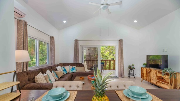 A modern living room with a brown sofa, a wooden TV stand, and a dining table set with plates and a pineapple. - Modern Apartment in West End (West End)
