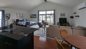 Ett rymligt vardagsrum med en stor säng, ett matbord och en soffa. Det finns en takfläkt, en tv och ett fönster med utsikt över omgivningen.