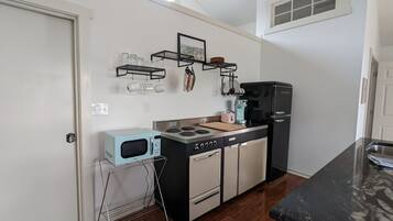 A compact kitchen with a microwave, stove, and coffee maker. There are shelves with cups and a small window above the sink.
