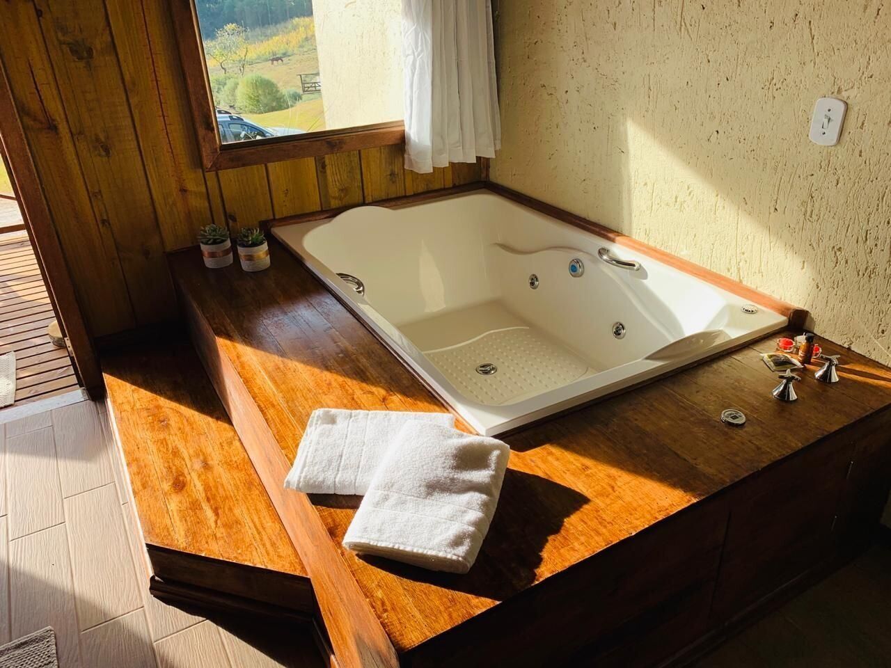 A wooden bathtub with a window view, a towel, and a small plant on the side.