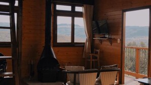 Un chalet confortable avec un intérieur en bois, une cheminée, une table avec des chaises et un balcon offrant une vue sur les montagnes.