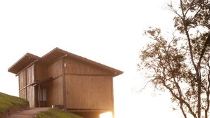 Une cabane en bois, dotée d’un toit en pente, située sur une colline herbeuse et offrant une vue sur le paysage.
