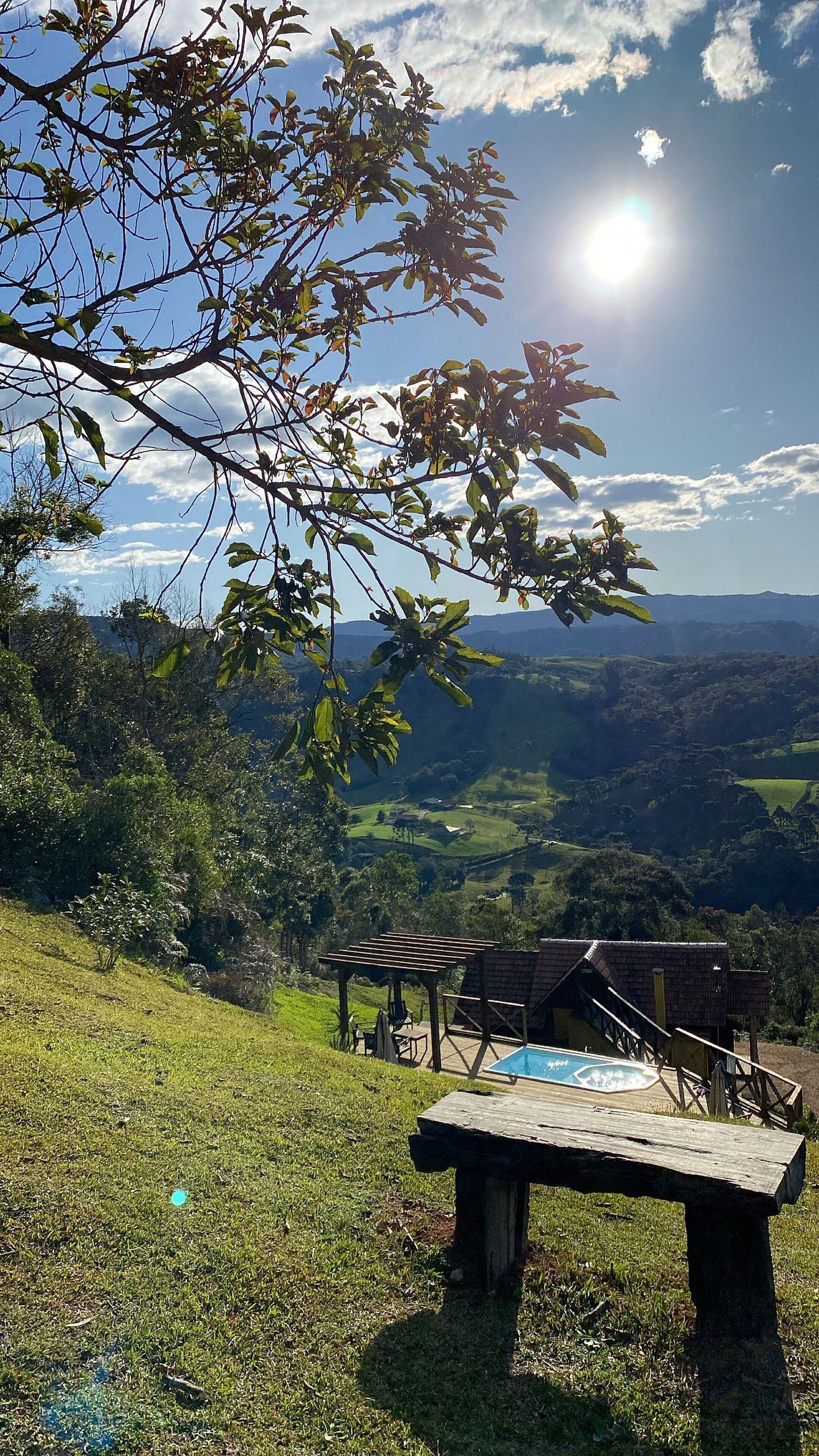 Un banco de madera con vistas a un valle pintoresco, cielo despejado y sol.