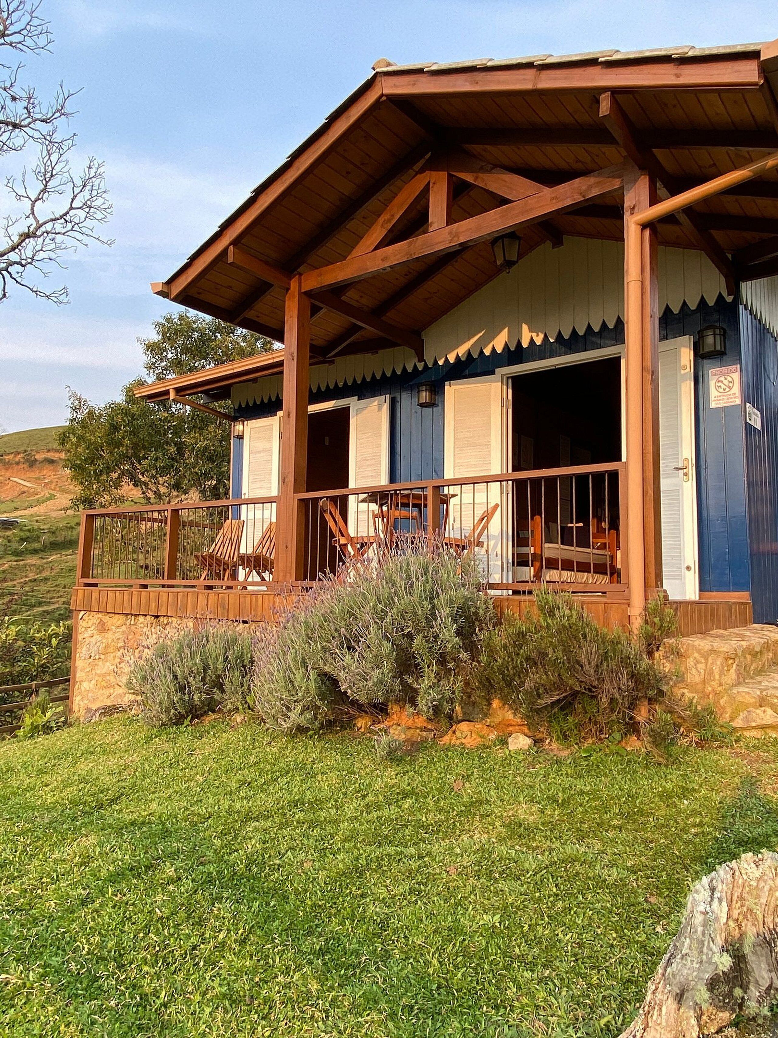 A rustic cabin with a wooden porch, stone foundation, and a view of the surrounding landscape.