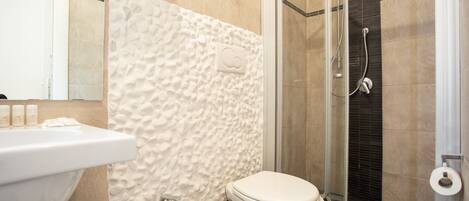 Un baño con lavamanos blanco, inodoro y zona de ducha con mampara de vidrio.