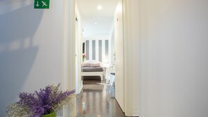 A hotel hallway leading to a bedroom with a bed, bedside table, and a nightstand. There is a green plant with purple flowers on the floor. - Romanticasa Navona  (Rome)