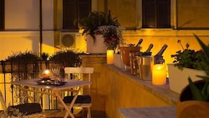 An outdoor dining area with a table set for two, surrounded by potted plants and candles. - Romanticasa Navona  (Rome)