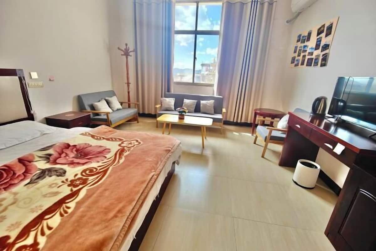 A hotel room with a bed, sofa, desk, TV, and a window with curtains.