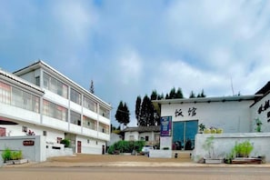 A building with a blue door and a sign above it. There are plants and a fence in front of the building. - Hongtu Qiufeng Inn (Kunming)