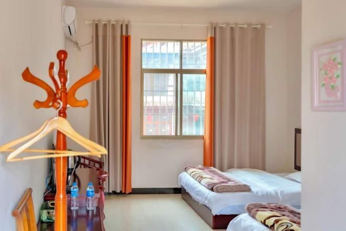 A hotel room with two beds, a wooden chair, a table with water bottles, and a window with curtains.