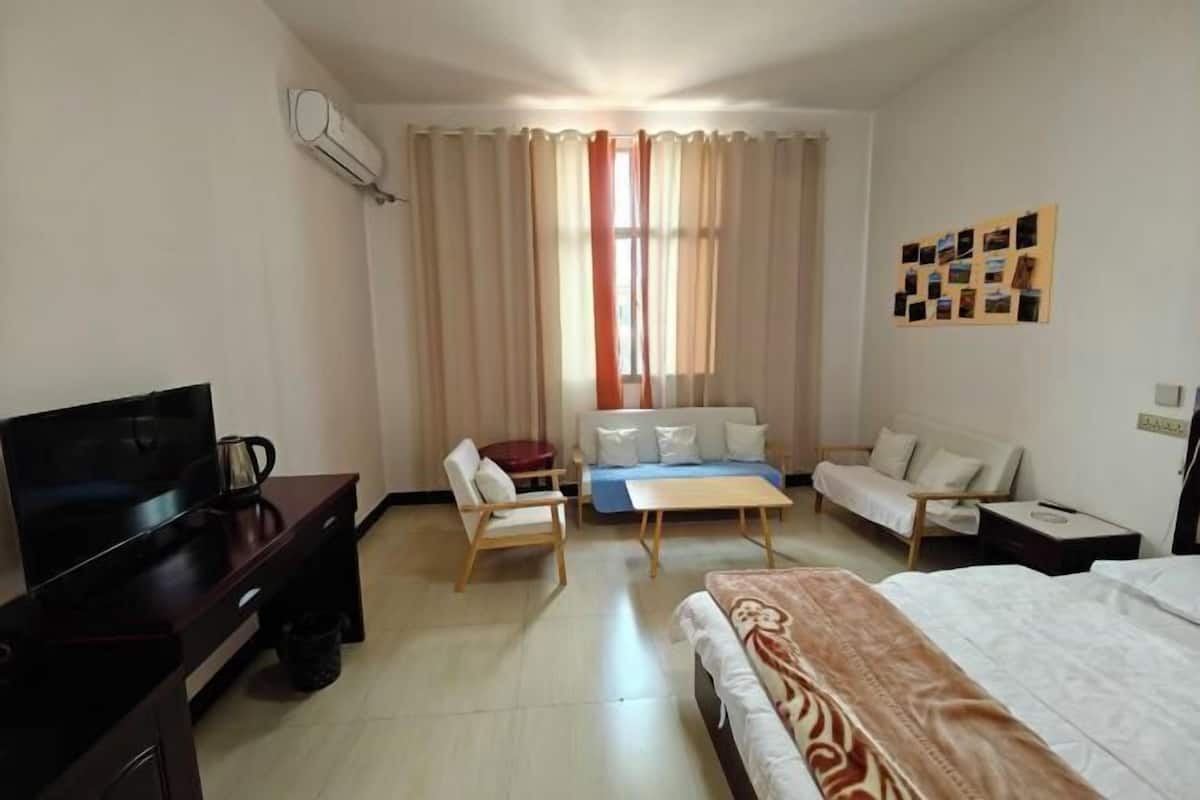 A hotel room with a bed, a desk with a TV, a sofa, a small table, and a window with curtains.