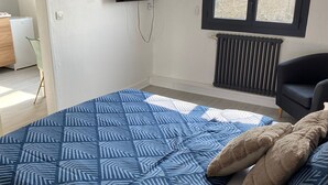 Et soveværelse med en seng, et fjernsyn ophængt på væggen, et vindue og en radiator.