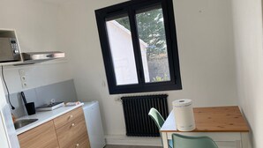 Et lille køkken med et vindue, et minikøleskab, en vask, et træskab, et bord med en stol og en radiator.