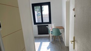 En smal gang med en radiator, et vindue og et bord med stole.