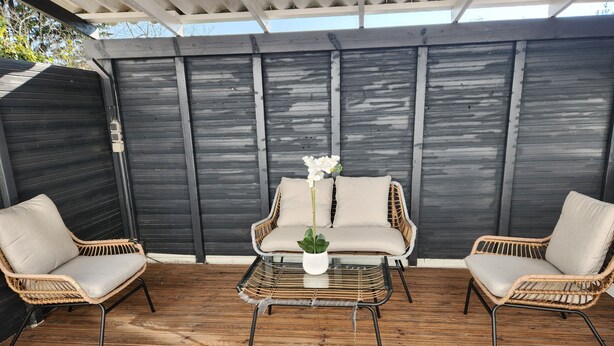 En udendørs terrasse med fletmøbler, et glasbord og en potteplante.