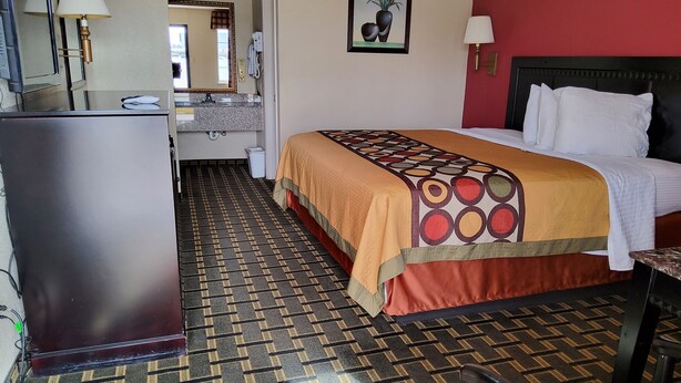 A hotel room with a bed, a desk, a chair, a refrigerator, a mirror, a bathroom, and a patterned floor. - Budget inn (Texarkana)