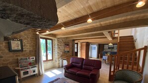 A spacious living area with a stone wall, wooden ceiling, a red leather sofa, a patterned rug, and a staircase leading to another level.