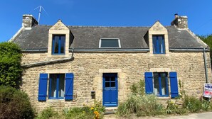 A stone building with two dormer windows and a small skylight, featuring blue shutters and a chimney.