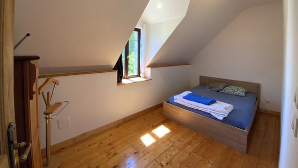 A bedroom with a sloped ceiling, a window, a bed, and a wooden floor.