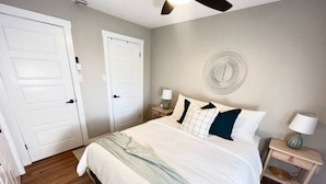 A bedroom with a large bed, two bedside tables with lamps, a ceiling fan, and a wall-mounted circular decoration. - Upper Unit 1067 Rawding  (Port Williams)