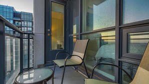 Ein Balkon mit zwei Stühlen, einem kleinen Tisch, großen Fenstern und Blick auf ein modernes Gebäude.