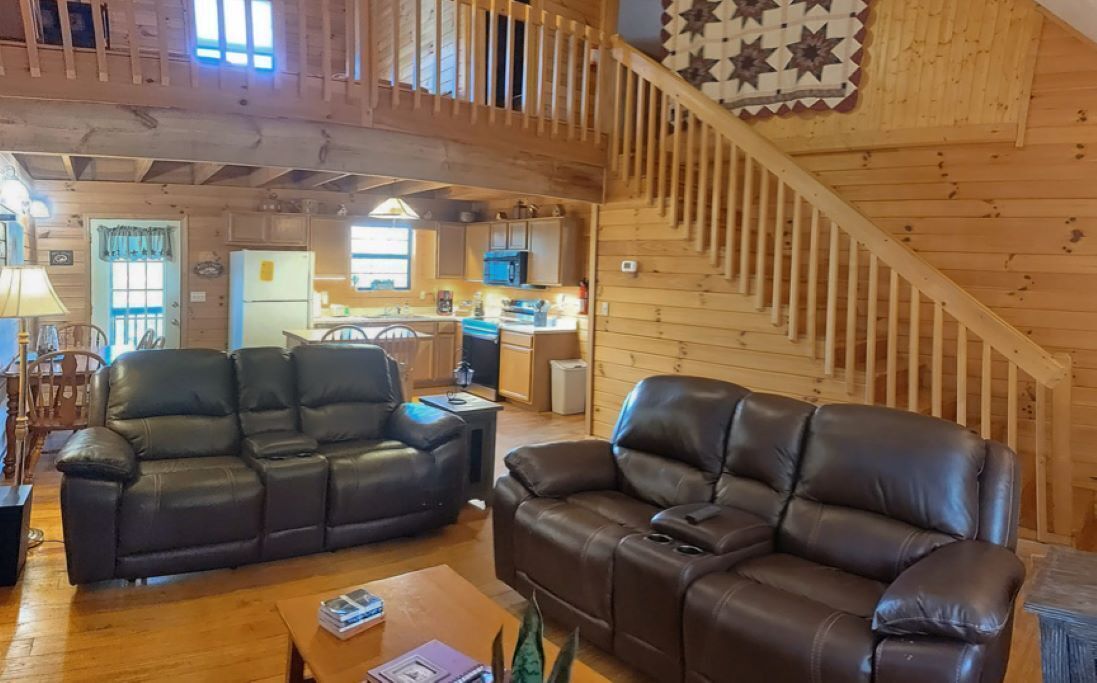 Een gezellig interieur van een chalet, met een zithoek met twee leren banken, een houten salontafel en een trap naar een hoger niveau.