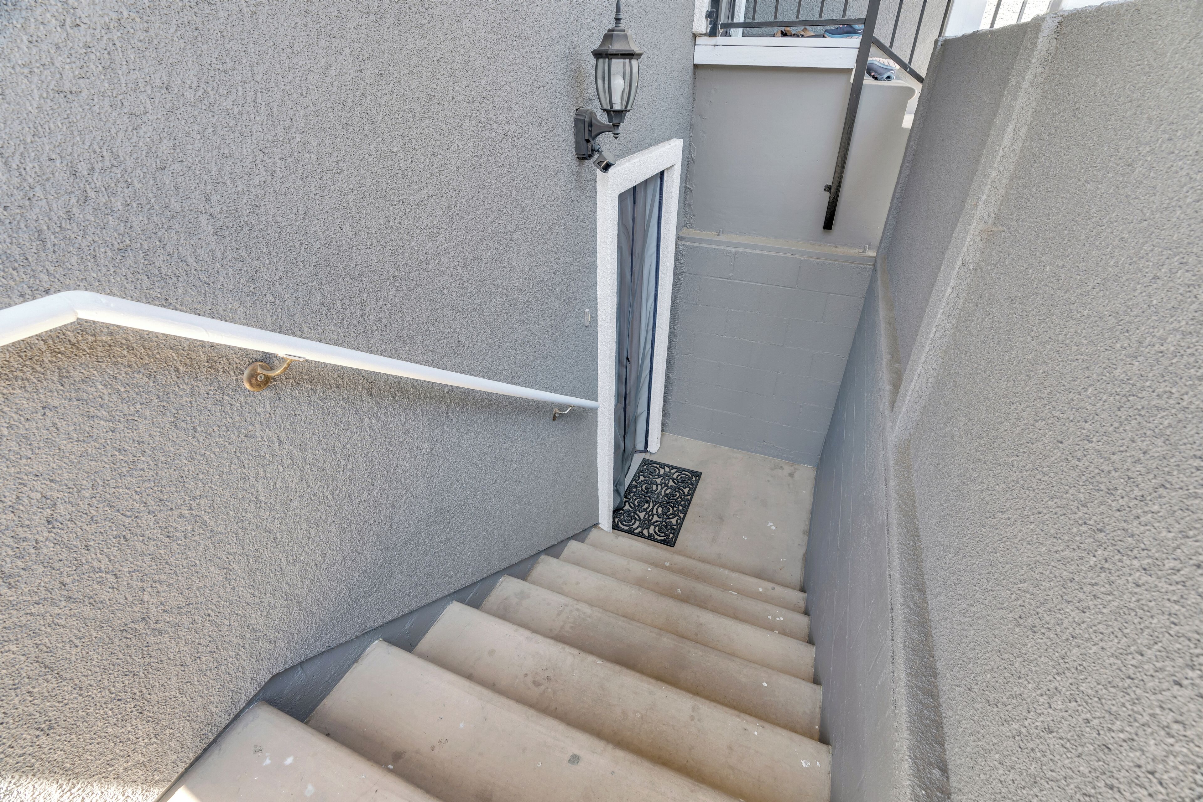 Un escalier étroit avec une rampe blanche, une porte en haut et un petit luminaire décoratif.