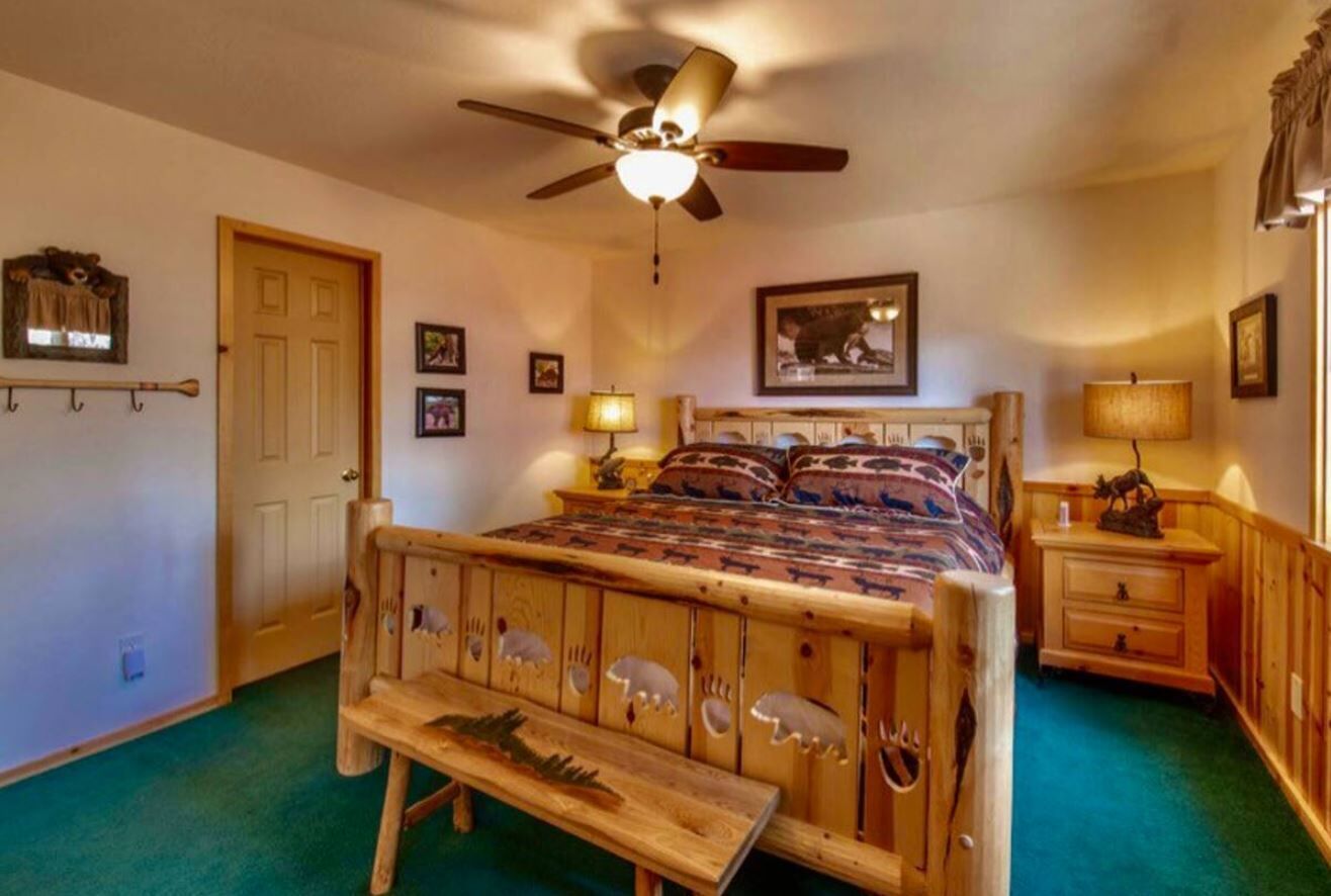 Un dormitorio con cama de madera, ventilador de techo, banca y mesita de noche con lámpara.
