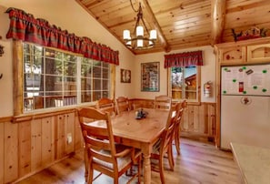 Une salle à manger en bois, avec une grande table et des chaises, des murs en bois et un plafond avec des poutres apparentes.