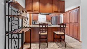 A kitchen with wooden cabinets, a stainless steel refrigerator, and two bar stools. - Spacious Private Vacation Home 3BR/2Bth - Family-sized, Big Backyard (Tallahassee)