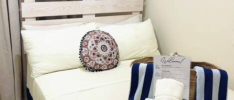 A neatly made bed with a white and blue striped towel, a decorative pillow, and a welcome sign.