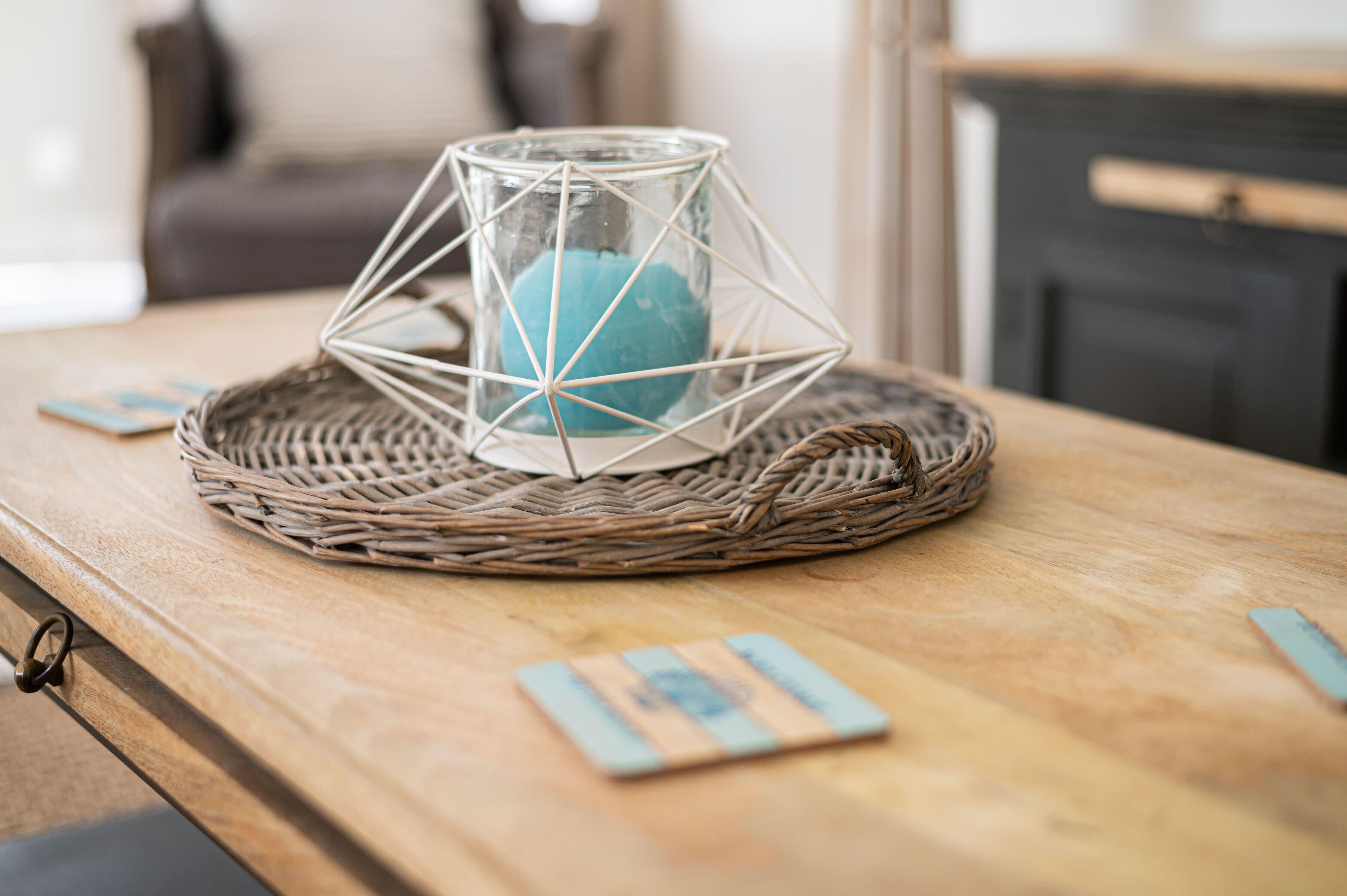 A wicker basket with a glass candle holder on a wooden table.