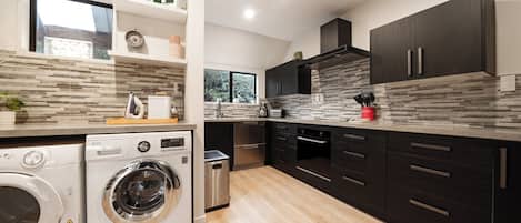 A modern kitchen with a built-in washer and dryer, dark cabinetry, and a stone backsplash.