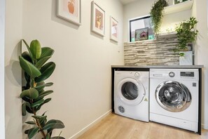 Une buanderie équipée de deux machines à laver à chargement frontal, d’un plancher en bois et d’une étagère murale agrémentée d’une plante.