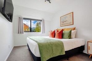 Quarto de hotel com cama, janela com cortinas, quadro na parede e televisão fixada na parede.