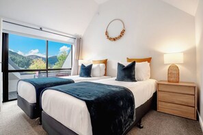 Une chambre d’hôtel avec deux lits, une grande fenêtre donnant sur la montagne, une table de chevet avec une lampe et un élément décoratif fixé au mur.