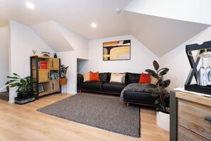 Uma sala de estar moderna com um sofá de couro preto, um tapete cinza e uma estante de madeira.