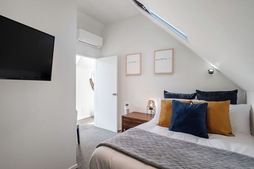 A bedroom with a bed, a flat-screen TV, a bedside table, and a wall-mounted light fixture.