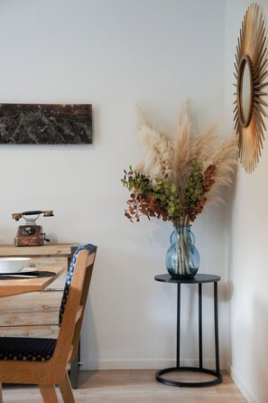 Un coin repas avec une table en bois, des chaises, un vieux téléphone à cadran, un vase contenant des plantes séchées et un miroir fixé au mur.
