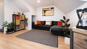 A modern living room with a black leather sofa, a wooden cabinet, and a large abstract painting on the wall. - Modern and Convenient apartment in Fernhill (Queenstown)