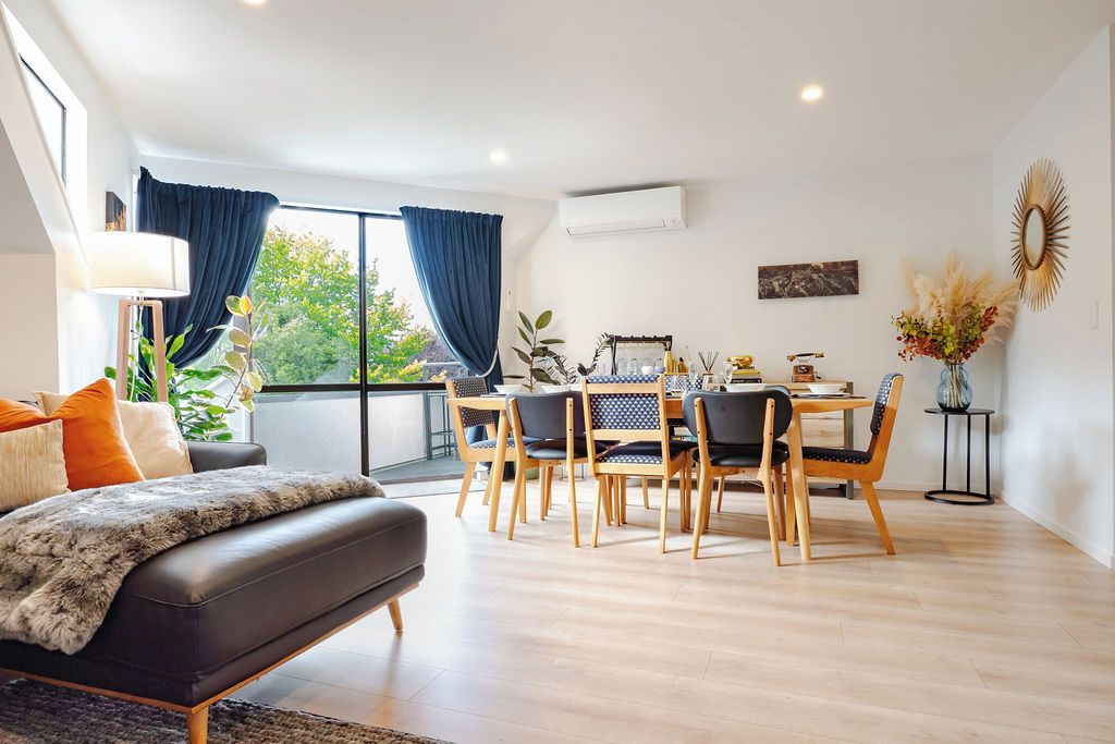 Ein modernes Wohnzimmer mit einer Couch, einem Esstisch und Stühlen. Es gibt ein großes Fenster mit Vorhängen, eine Lampe und eine Pflanze.