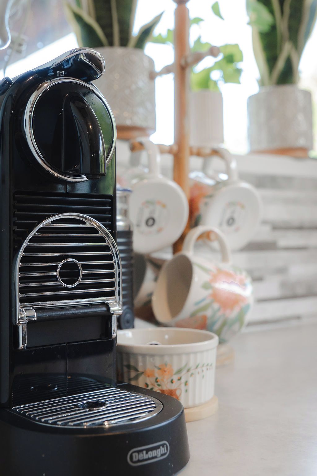 Una macchina per espresso DeLonghi su un bancone della cucina, con una tazza decorata con fiori e una tazza bianca sullo sfondo.