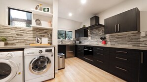 A modern kitchen with a washing machine, dark cabinets, and a tiled backsplash. - Modern and Convenient apartment in Fernhill (Queenstown)